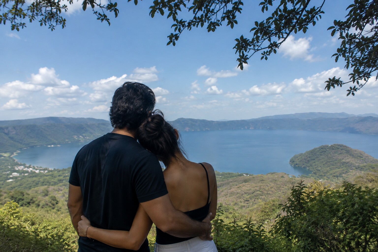 Happy couple embracing while looking at the real view of Lake Coatepeque from above in El Salvador