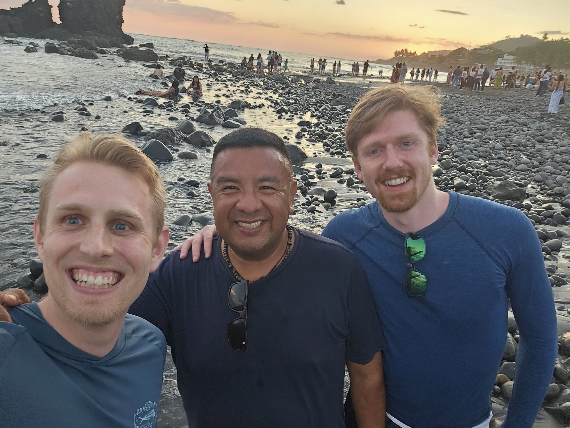 Three friends smiling on El Tunco black-sand beach at sunset
