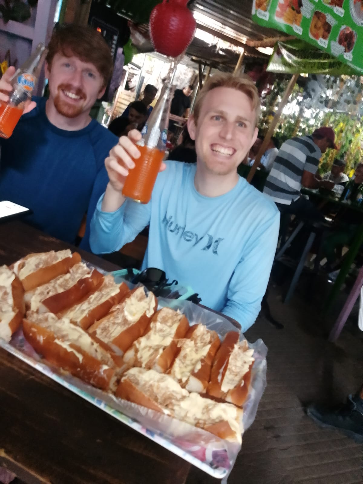 Two travelers laughing over sandwiches and sodas at a Salvadoran market