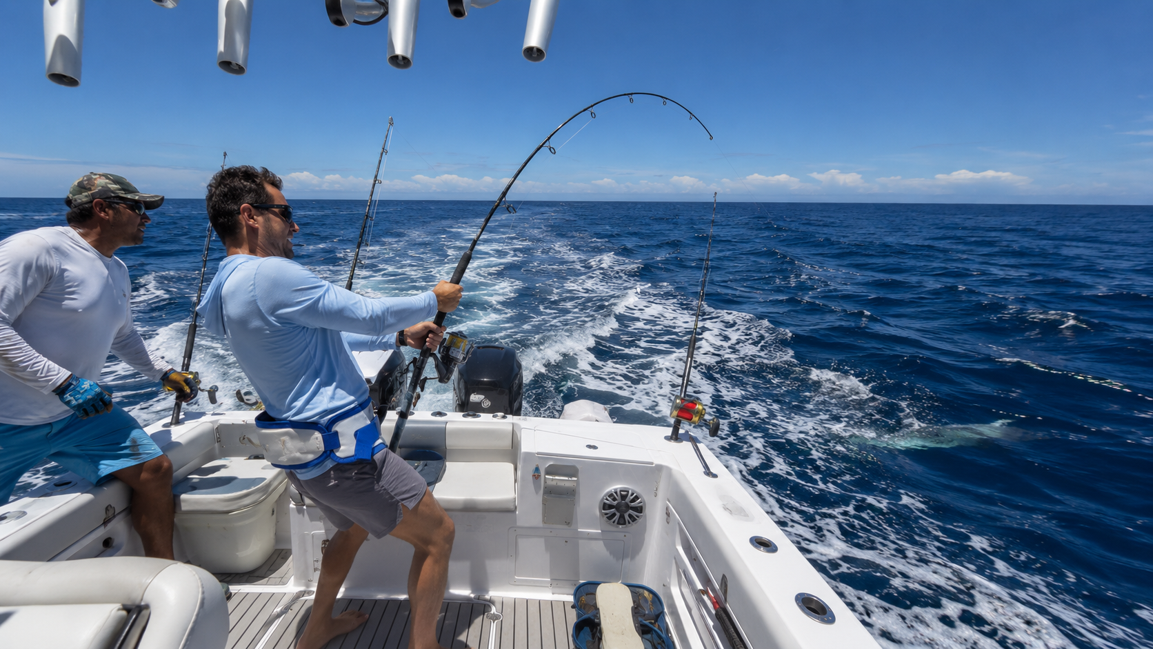 Two men fighting a fish on rods aboard a sport fishing boat in the open Pacific off El Salvador