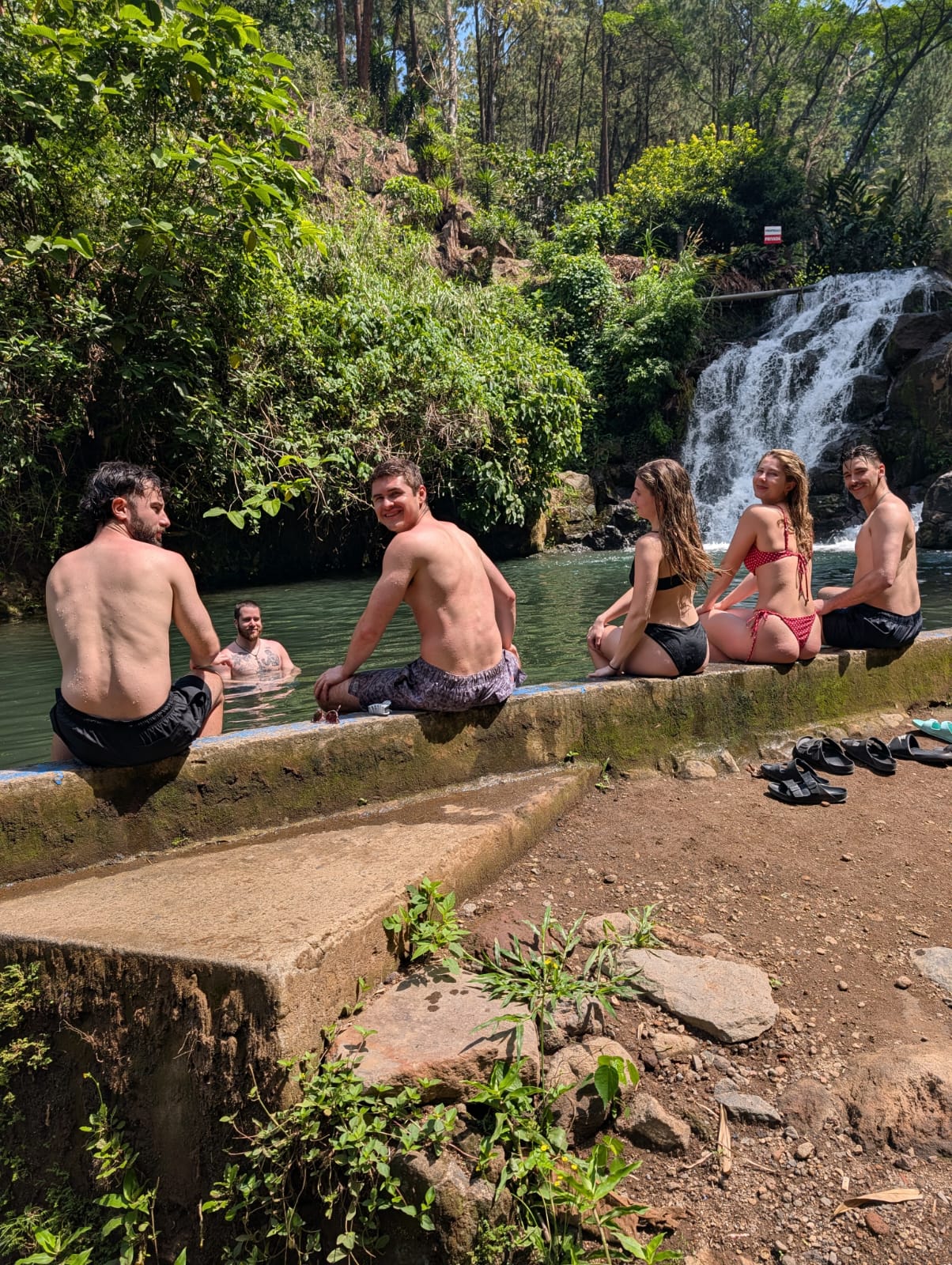 Friends swimming together at a natural river pool with a waterfall behind