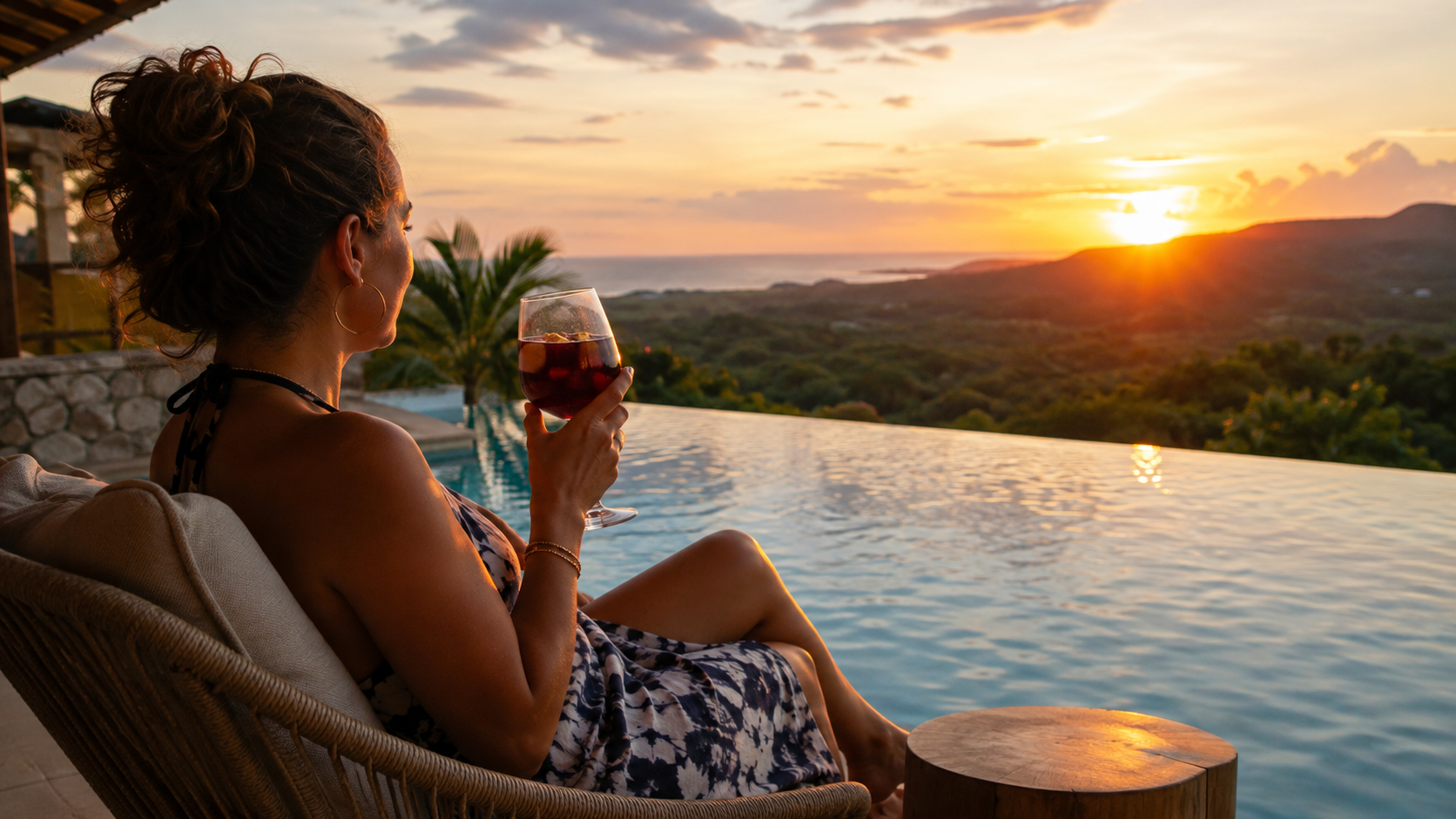 Woman relaxing in a chair beside an infinity pool at sunset in El Salvador, holding a glass of Sangría De la Casa with the Pacific coast in the distance