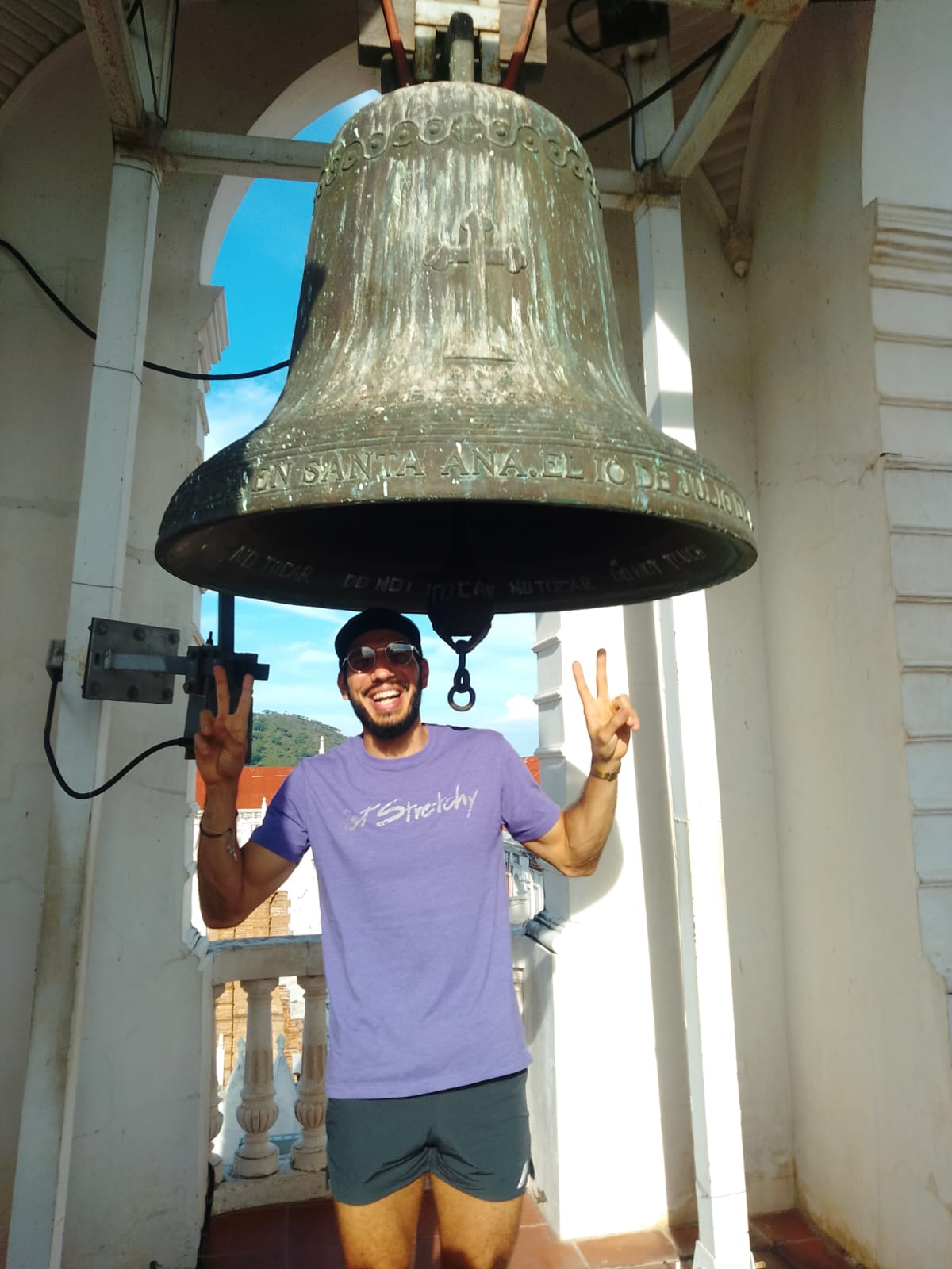 Traveler standing beneath the historic bronze bell of the Santa Ana Cathedral bell tower